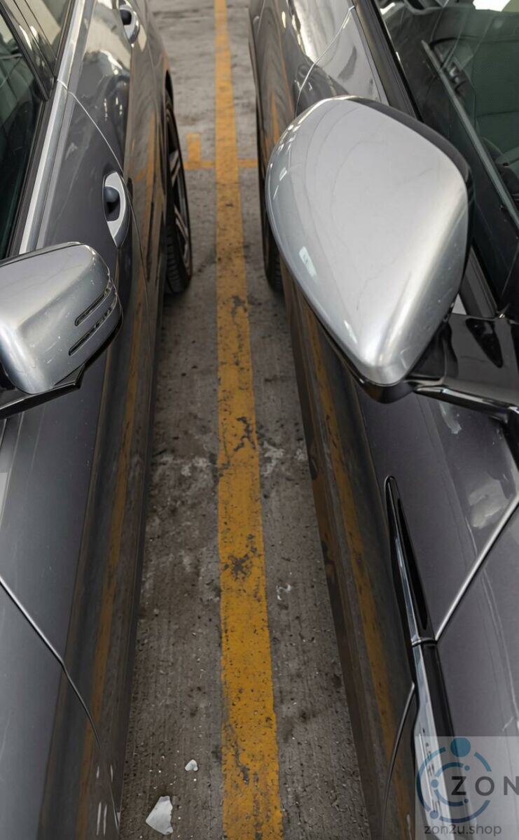 Two cars parked very close together with side mirrors nearly touching over a yellow line