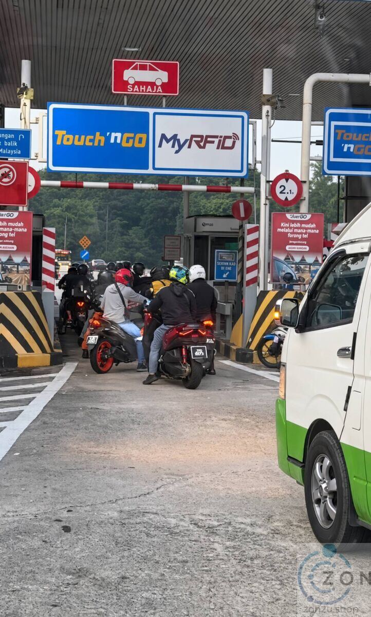 Motorcyclists queued at a Malaysian highway toll booth under a Touch 'n Go and MyRFID lane sign