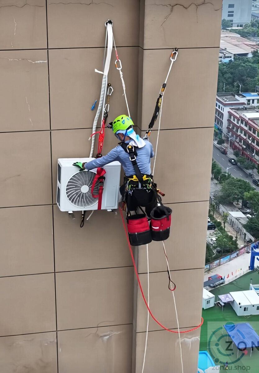 Technician suspended in a safety harness installing an outdoor air conditioner unit on a high-rise building